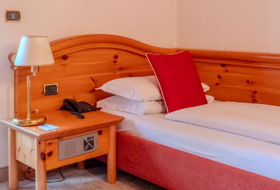 Camera accogliente con letto singolo, cuscino rosso e comodino in legno.