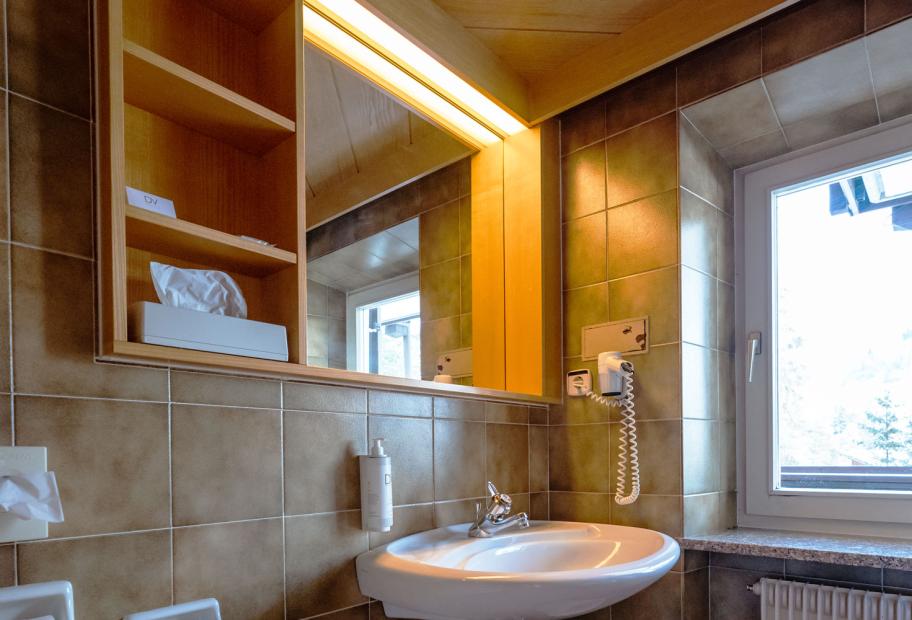 Bagno moderno con specchio illuminato, lavandino, e finestra.