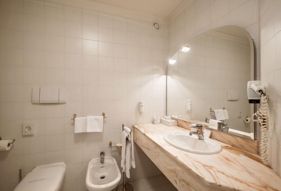 Bagno luminoso con lavabo, bidet, asciugacapelli e specchio grande.