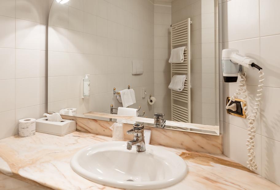 Bagno moderno con lavabo, specchio, phon e asciugamani.